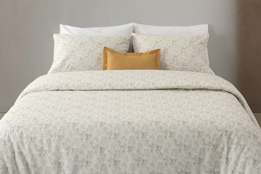 Almofada com estampado floral em preto e branco sobre fundo branco, disposta em cima de outra almofada amarela, num conjunto de roupa de cama com padrão floral.