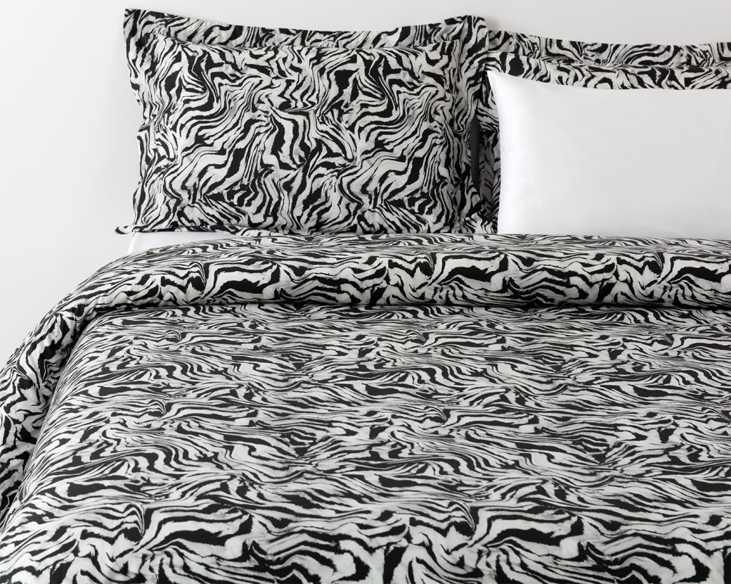 Bedding with a black and white animal print pattern inspired by zebra stripes, matching pillows, and an additional plain white cushion.​