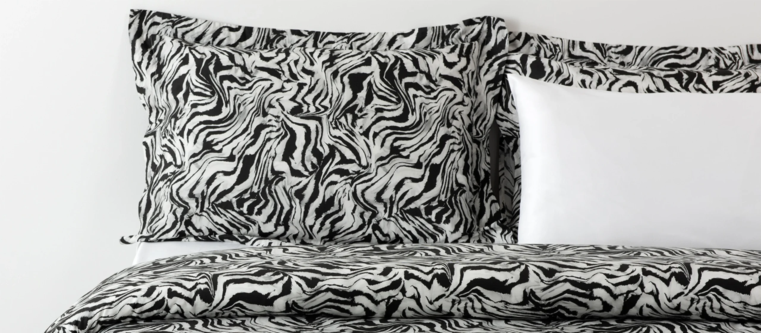 Cama com produtos da RIFER, destacando-se o padrão de zebra a preto e branco nas almofadas e capa de edredão