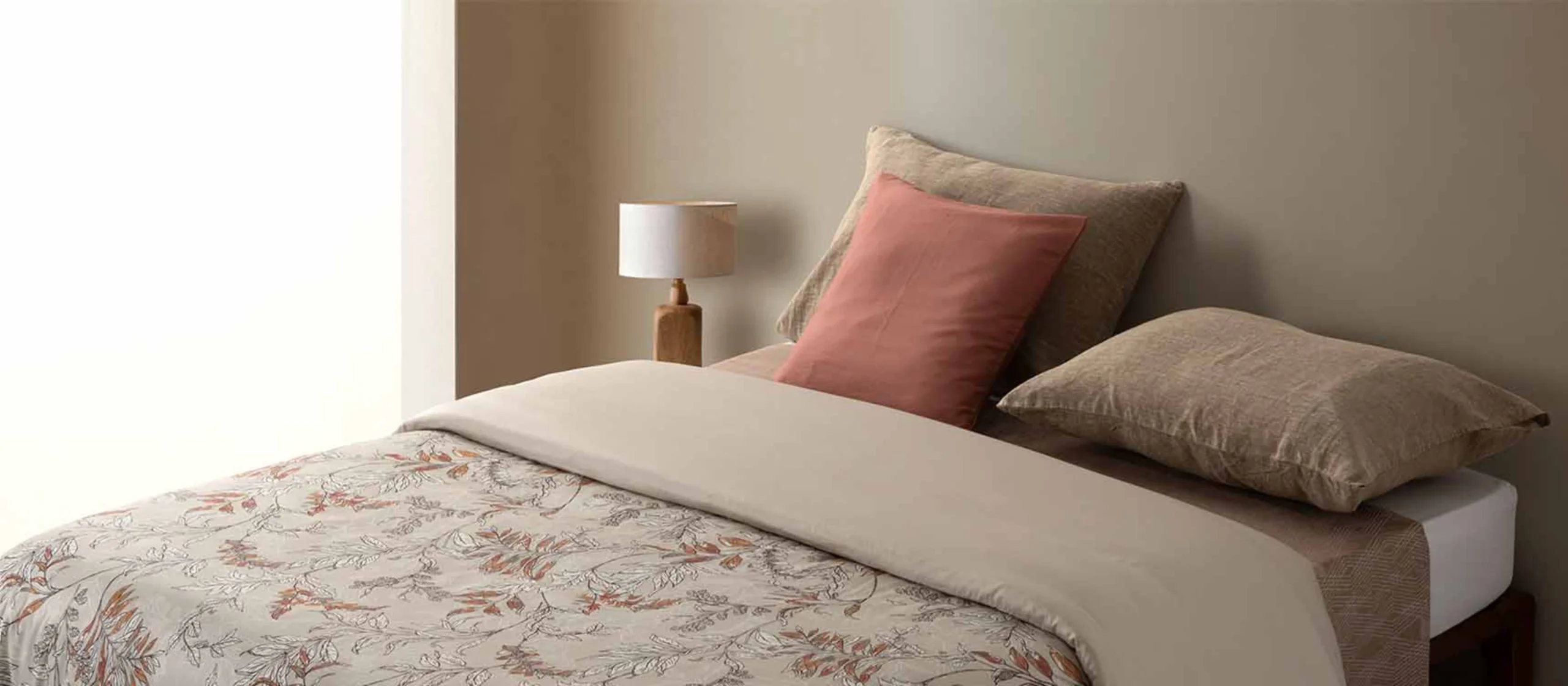 Cama com roupa de cama com padrão floral em tons de bege e almofadas em tons neutros e cor-de-rosa da RIFER.